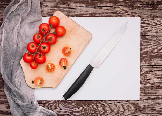 Free Photo sharp knife and bunch of cherry tomatoes on chopping board over the white paper against desk