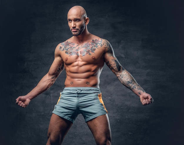 Free photo shaved head shirtless muscular male with tattooed body dressed in a sport short over grey background.