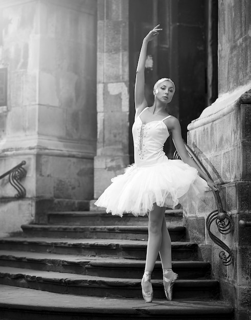 Free Photo she is a living art. vertical monochrome shot of a beautiful ballerina standing in ballet pose on stairs of an old castle soft focus