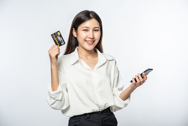 She was dressed in a white shirt and dark pants to go shopping and hold a credit card and smartphone