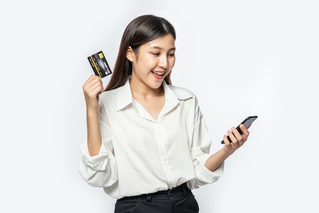 She was dressed in a white shirt and dark pants to go shopping and hold a credit card and smartphone