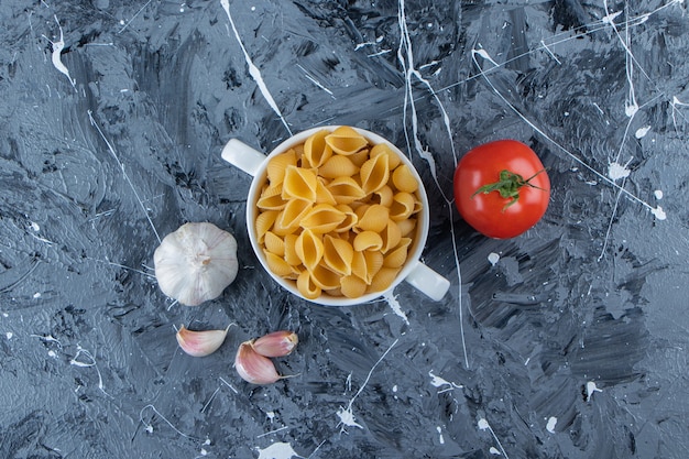 Shell uncooked pasta in a bowl with fresh red tomatoes and garlic . 