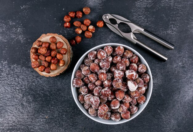 Shelled hazelnuts in a white bowl with piece of wood top view on a dark stone table