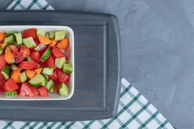 Shepherd's salad mixed with carrot slices on a navy platter on marble background. 