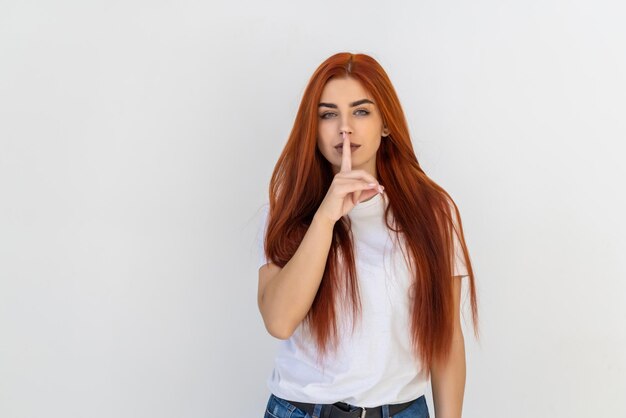 Shh, silence. Closeup redhead curly happy young woman placing finger on lips asking to be quiet isolated gray