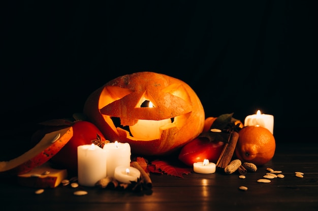 Free Photo shiny candles, cinnamon and fallen leaves stand before scarry halloween pumpkin