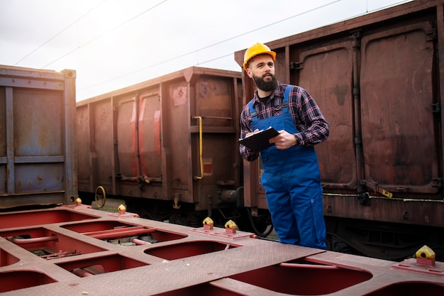 Free photo shipping railroad worker with clipboard keeping track of cargo containers ready to leave the train station