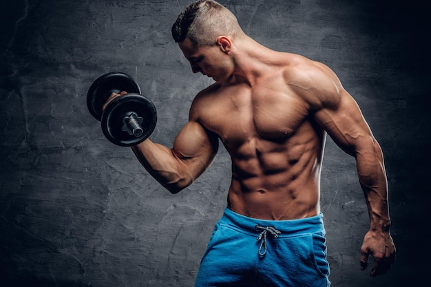 Free photo shirtless athletic male doing biceps workouts with one dumbbell on grey vignette background.