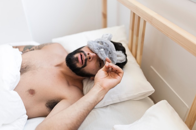 Shirtless man lying on bed peeking from an eye mask