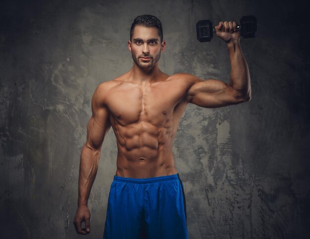 Shirtless muscular guy holding dumbell on grey background