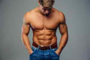 Free photo shirtless muscular young man in denim jeans with hands in pockets. isolated on grey background.