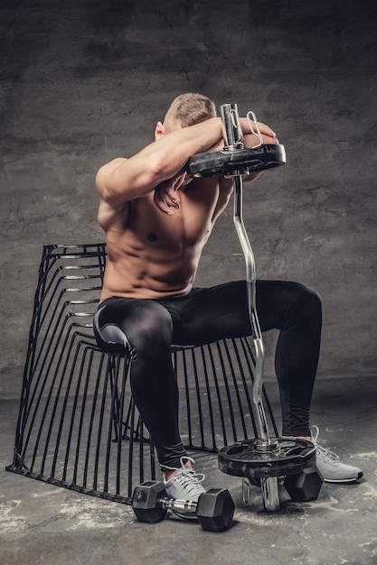 Free photo shirtless sporty male sitting on a chair and holding barbell.