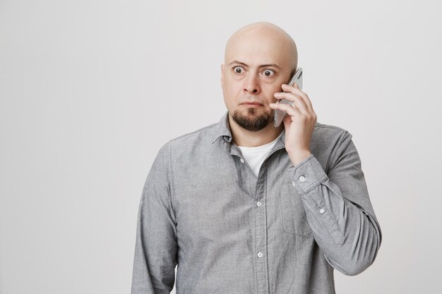 Shocked adult bald guy answer strange phone call