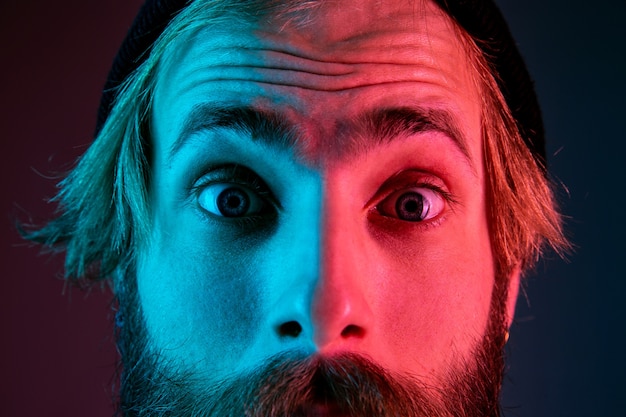 Free photo shocked, astonished, close up. caucasian man's portrait on gradient studio background in neon light. beautiful male model with hipster style. concept of human emotions, facial expression, sales, ad.