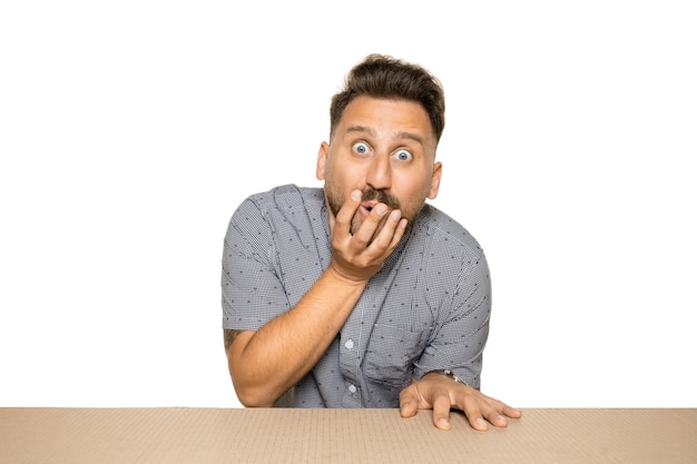 Free photo shocked and astonished man opening the biggest postal package. excited young male model on top of cardboard box looking inside.