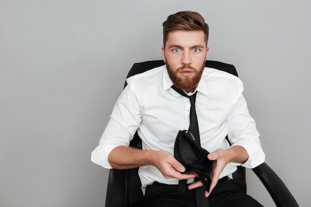 Shocked bearded man in white shirt showing empty wallet