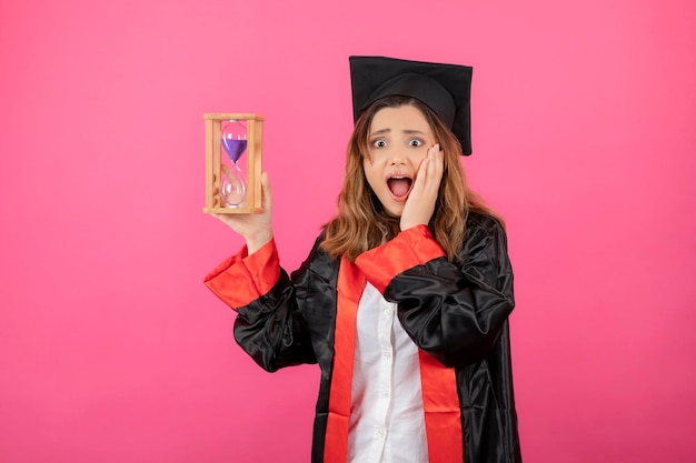 Free photo shocked beautiful female student holding time clock put her hand to her face. high quality photo