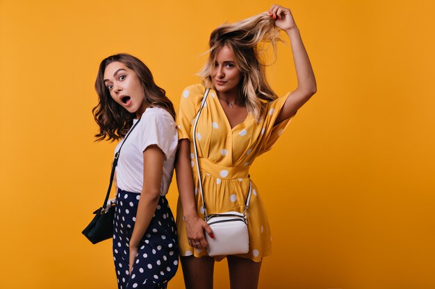 Shocked curly brunette girl spending time. Wonderful fair-haired tanned woman chilling with friend.