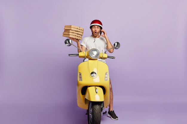 Shocked deliveryman driving scooter while holding pizza boxes