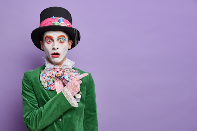 Free Photo shocked embarrassed hatter on masquerade party indicates at upper right corner stunned by something horrible isolated over purple wall shows empty space for your information