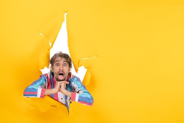 Shocked and emotional young man in torn yellow paper hole background