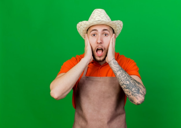 Free photo shocked gardener man wearing gardening hat puts hands on face looking