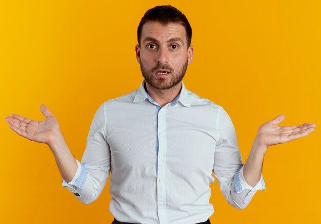 Shocked handsome man stands with open hands isolated on orange wall