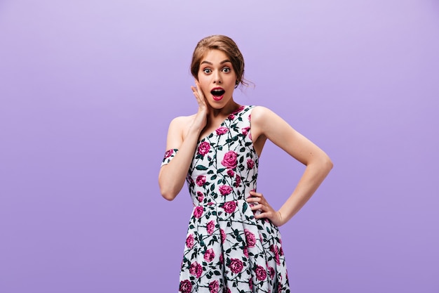 Free photo shocked lady in floral dress poses on isolated background. surprised young woman with red lips in stylish clothes looking into camera.