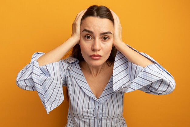 Shocked pretty woman holds head isolated on orange wall