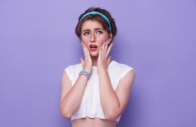 Shocked and scared young woman covering her mouth standing isolated over purple studio background