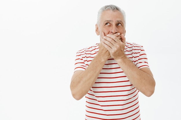 Shocked senior man shut mouth concerned and looking upper left corner