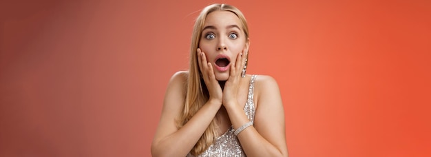 Free photo shocked speechless concerned young stunned woman gasping screaming worried drop jaw touch cheeks widen eyes surprised nervously staring camera troubled afraid standing red background