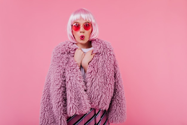 Free photo shocked stunning woman in bright sunglasses posing . emotional girl in fluffy jacket and peruke isolated on pink wall with surprised face expression