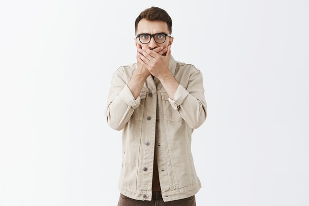 Shocked and surprised bearded man in glasses posing against the white wall