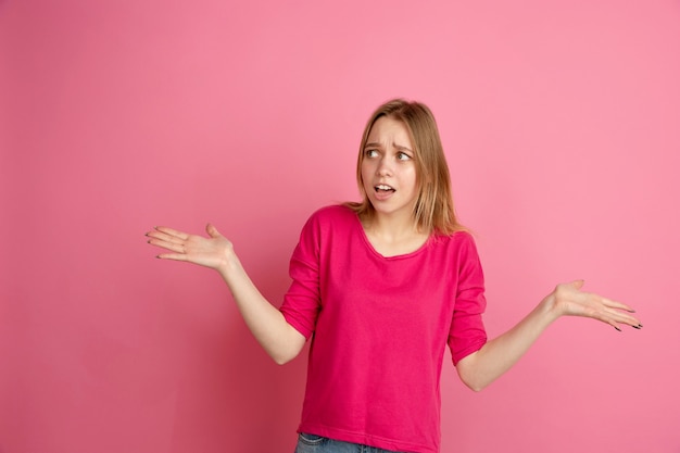 Shocked, uncertain. Caucasian young woman's portrait isolated on pink  wall, monochrome. Beautiful female model. 