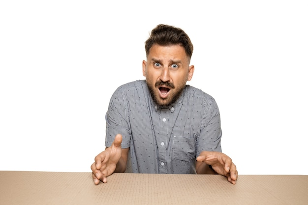 Shocked and upset man on biggest postal package. Sad and disappointed young male model on top of cardboard box looking inside.