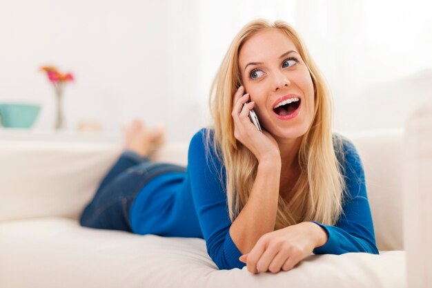 Shocked woman lying down on sofa and talking on the phone 
