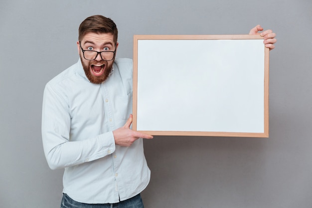 Free photo shocked young bearded businessman holding blank board