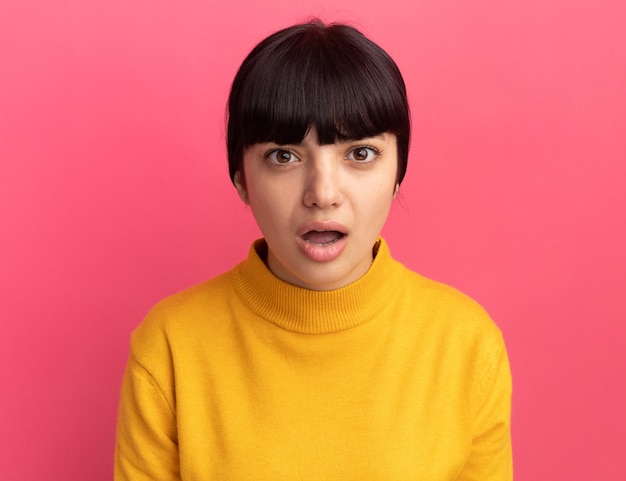 Shocked young brunette caucasian girl isolated on pink wall with copy space