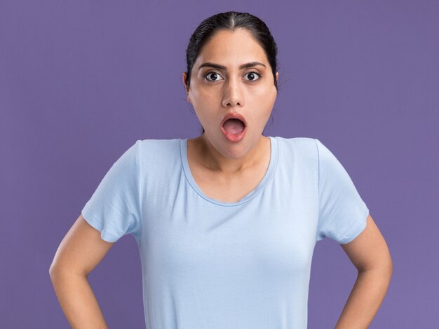 Shocked young brunette caucasian girl looking at camera on purple