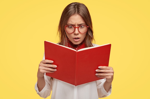 Free photo shocked young brunette with glasses posing against the yellow wall