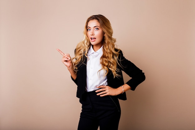 Free photo shocked young business woman or employe in stylish suit posing over beige wall.