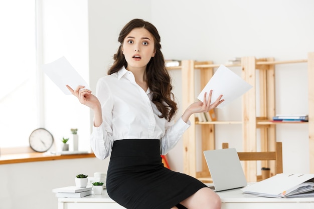 Shocked young business woman surprised by reading unexpected news in document amazed woman office worker feeling stunned baffled by unbelievable information in paper about debt or dismissal