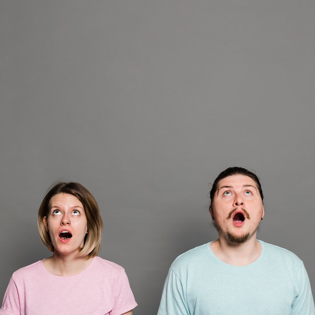 Shocked young couple with their mouth opened looking up against grey wall