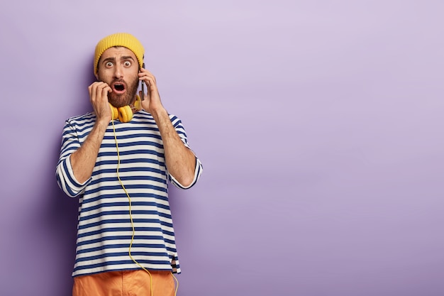 Free photo shocked young man makes order via cellular, stunned he cannot book table in restaurant, looks with omg expression, wears fashionable outfit