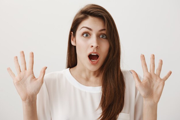 Shocked young woman scream and lift hands up in surrender