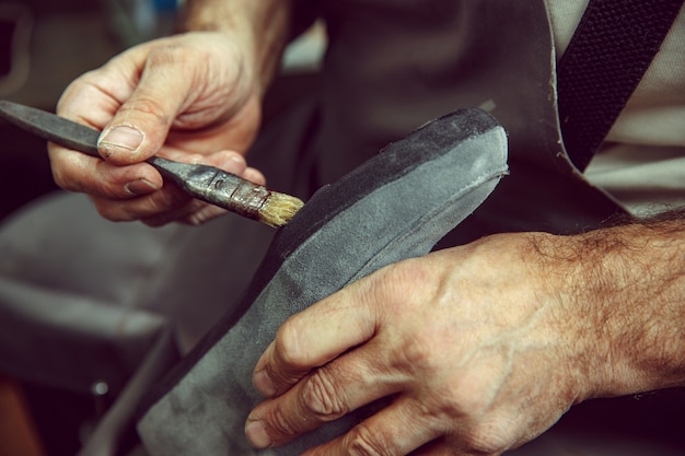 Shoemaker makes shoes for men. He smears special liquid with a brush. The man in female profession. Gender equality concept