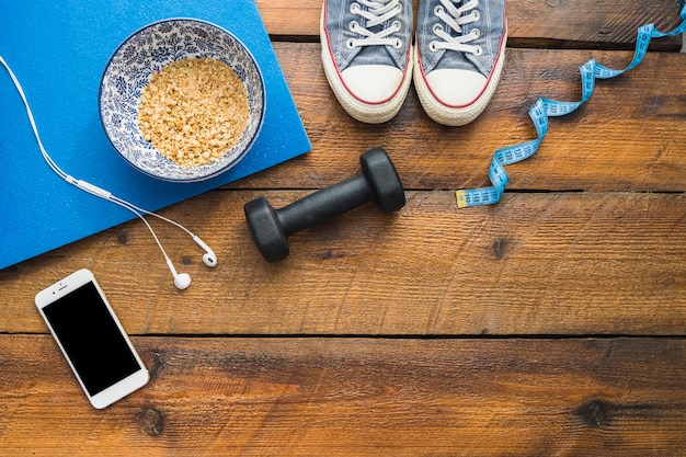 Shoes; measuring tape; dumbbell; earphone; cellphone and bowl of oats on wooden textured table