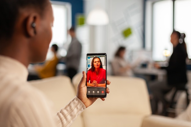 Free photo over the sholder of black employee discussing with partner on video call using phone in start up business office