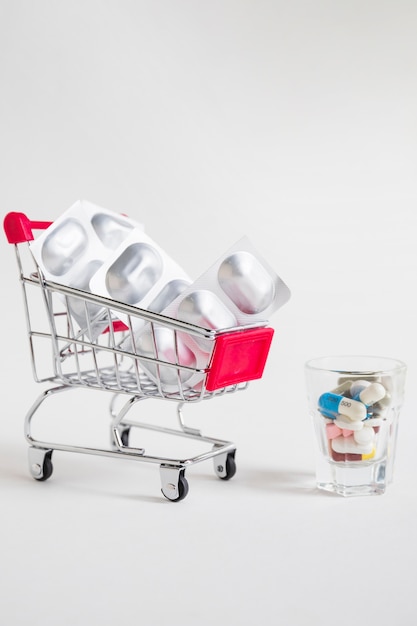 Free photo shopping cart with pill blister and medicines in glass on white background